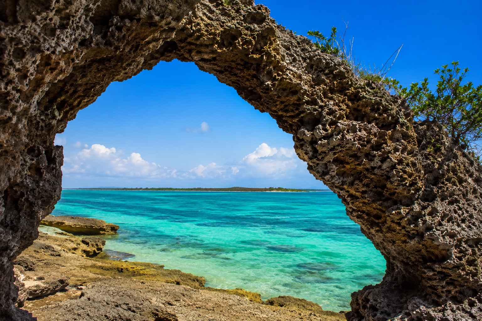 Ibo Island coral stone archway framed by tropical vegetation with turquoise Quirimbas Archipelago waters visible beyond, Mozambique heritage honeymoon destination, editorial photography