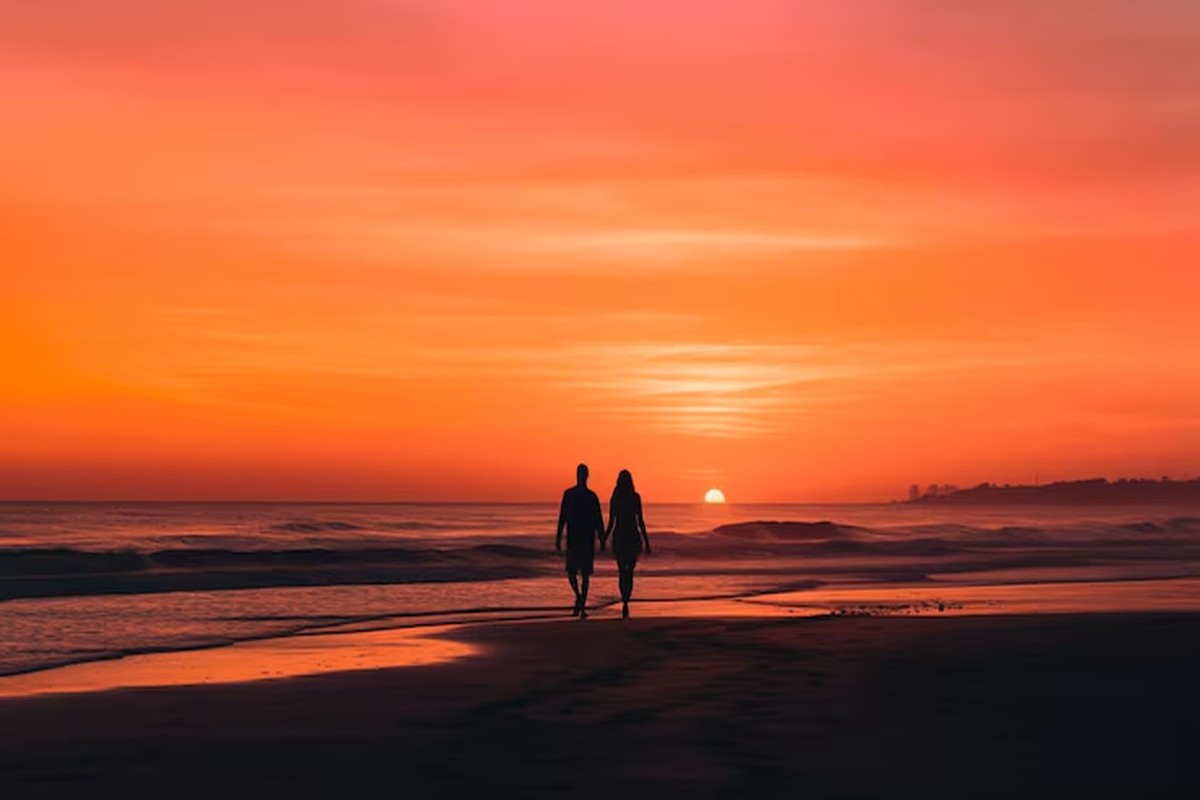 Two figures walking along an empty white-sand beach at low tide in the Bazaruto Archipelago with shallow turquoise water reflecting soft morning light, romantic Mozambique honeymoon, editorial photography