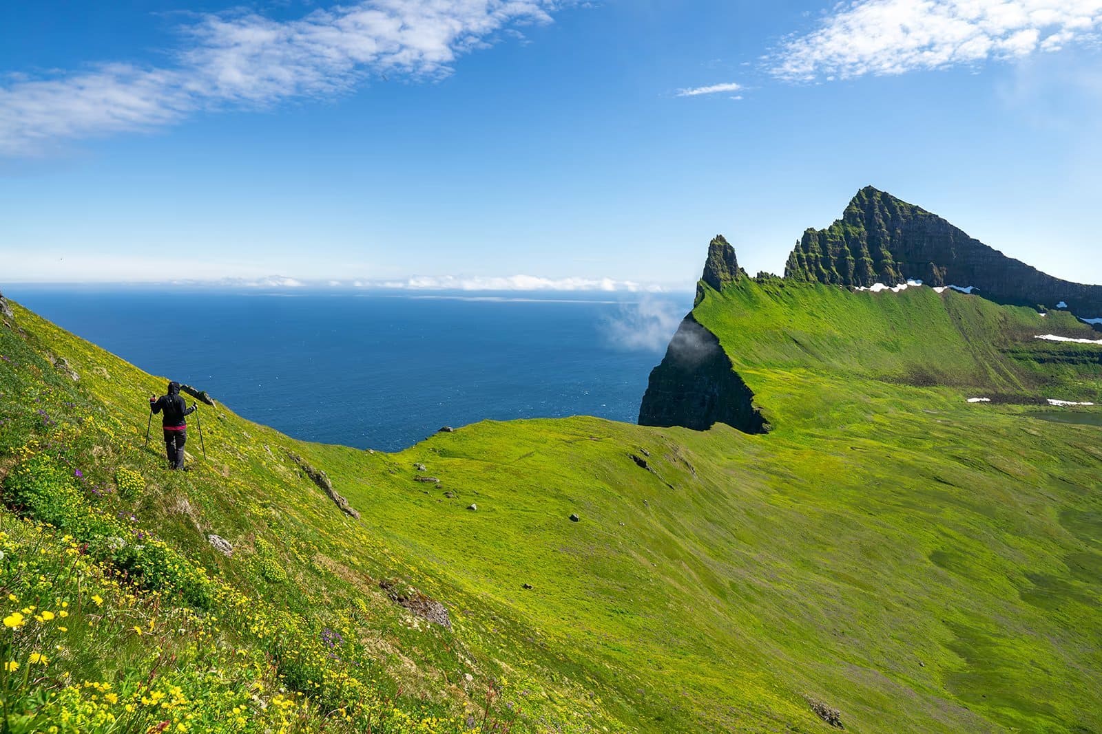 Westfjords coastline in Iceland with steep sea cliffs dropping into turquoise fjord water and a remote gravel road winding along the cliff edge, off-the-beaten-path honeymoon, editorial photography