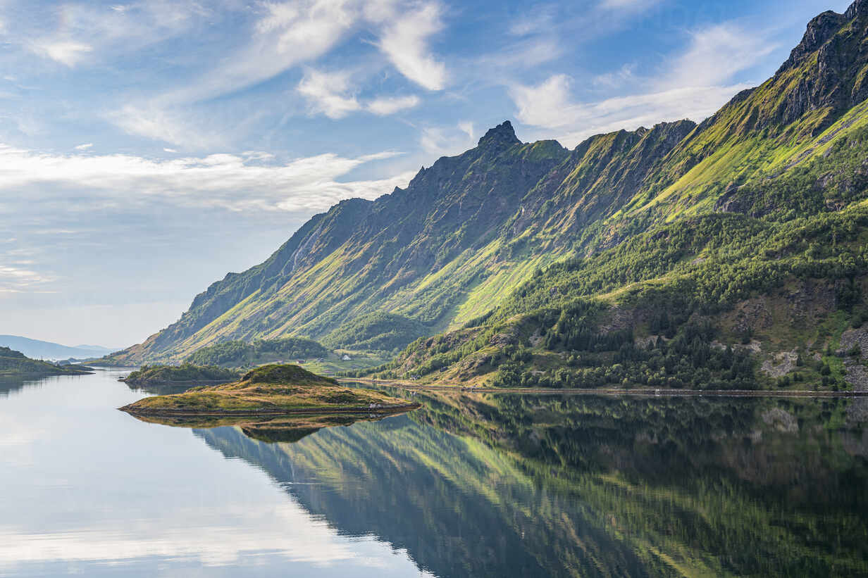 Norwegian fjord at dawn with mirror-still turquoise water reflecting steep green mountains and low morning mist, serene Scandinavian honeymoon landscape, editorial travel photography