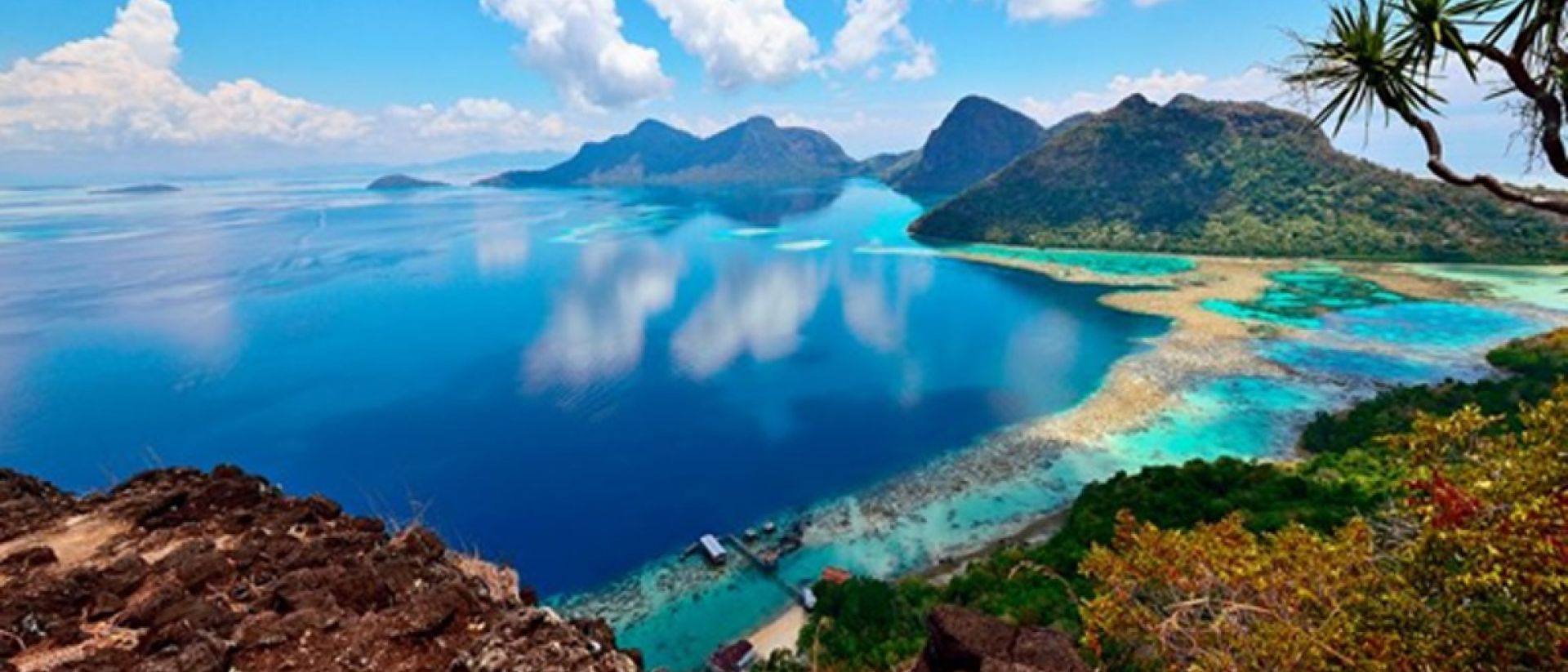Turquoise tropical water surrounding a small coral island off the Sabah coast in Borneo with white sand beach and lush green vegetation, island finale honeymoon, editorial travel photography