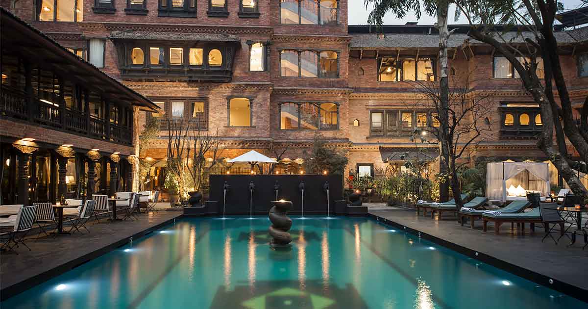 Courtyard of Dwarika's Hotel in Kathmandu with carved wooden columns and traditional Newari architecture surrounding a peaceful garden, luxury heritage honeymoon accommodation, editorial photography