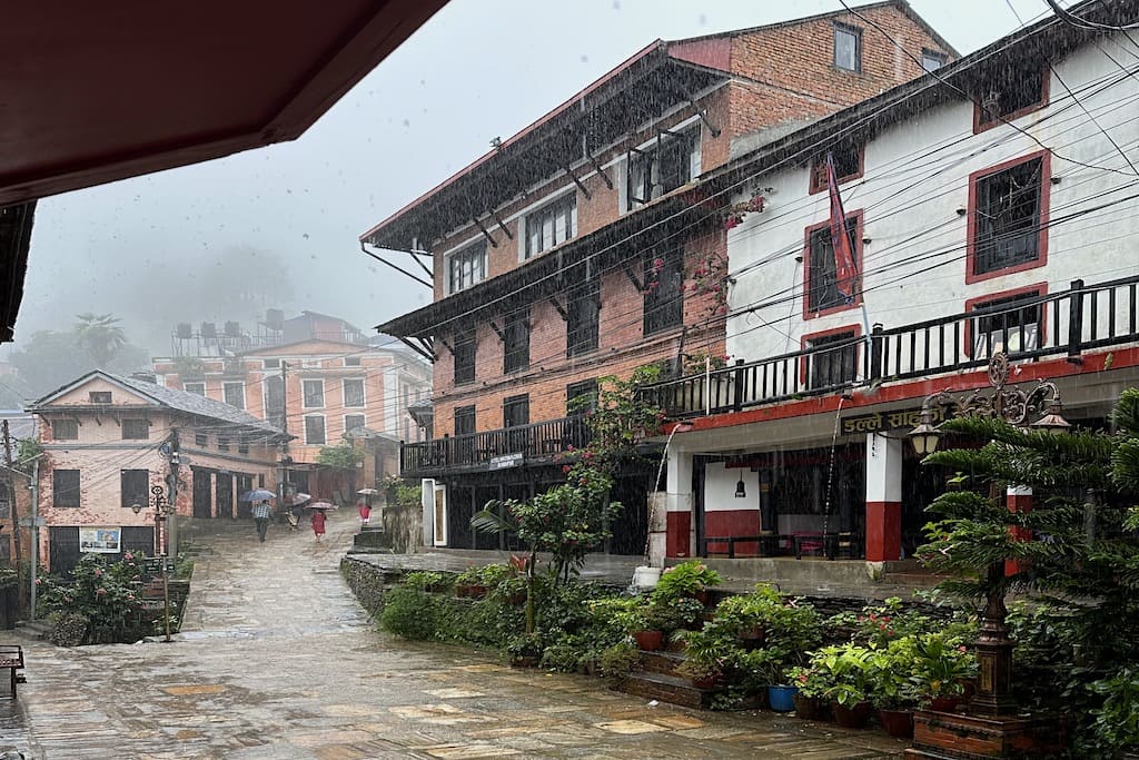 Quiet cobblestone main street of Bandipur village in Nepal with traditional Newari brick buildings and prayer flags stretching between rooftops against a mountain backdrop, hidden gem honeymoon stop, editorial photography