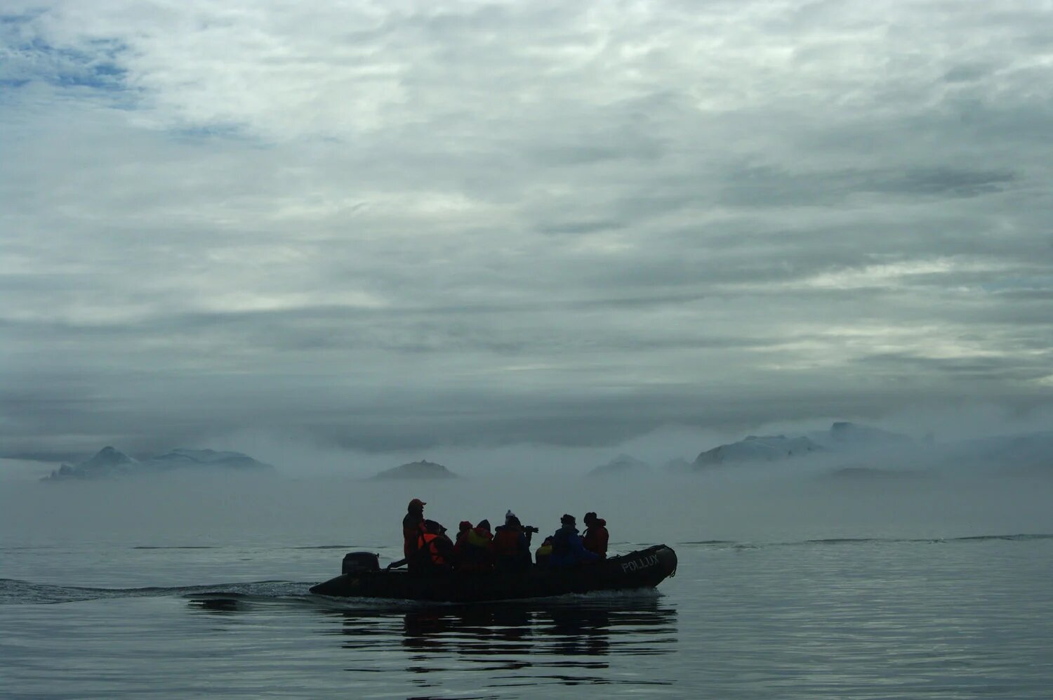 Zodiac boat navigating between towering blue icebergs in Disko Bay Greenland with passengers observing the ice from close range under soft Arctic light, expedition honeymoon experience, editorial photography
