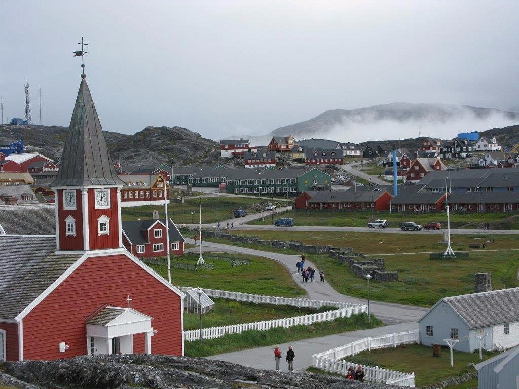 Colourful houses of Nuuk Greenland's capital city built along a rocky harbour with fishing boats and calm fjord water reflecting mountain backdrop, Arctic capital honeymoon, editorial photography