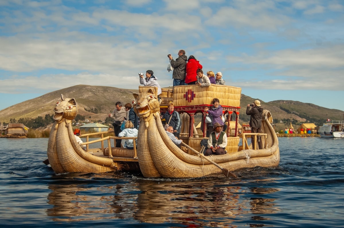 Traditional reed boat on Lake Titicaca Bolivia with deep blue water and distant snow-capped Andean peaks under a vast sky, high altitude cultural honeymoon, editorial travel photography