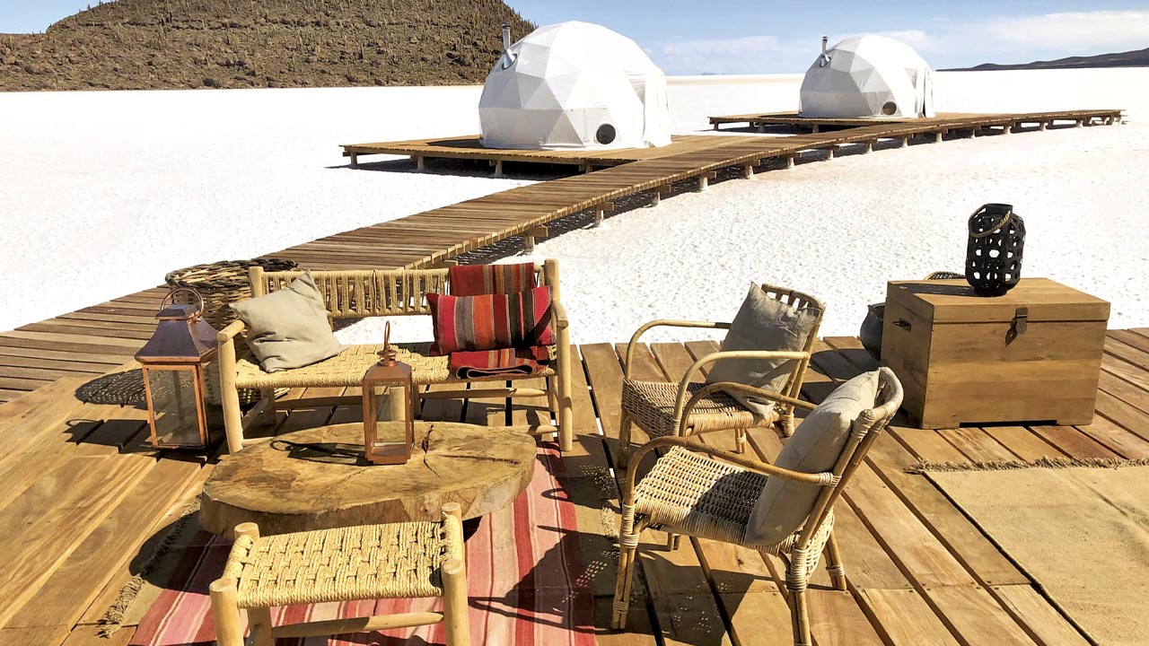 Geodesic dome lodge on the edge of Salar de Uyuni at sunset with pink sky reflecting on the white salt flat and distant volcanic peaks, luxury Altiplano honeymoon accommodation, editorial photography