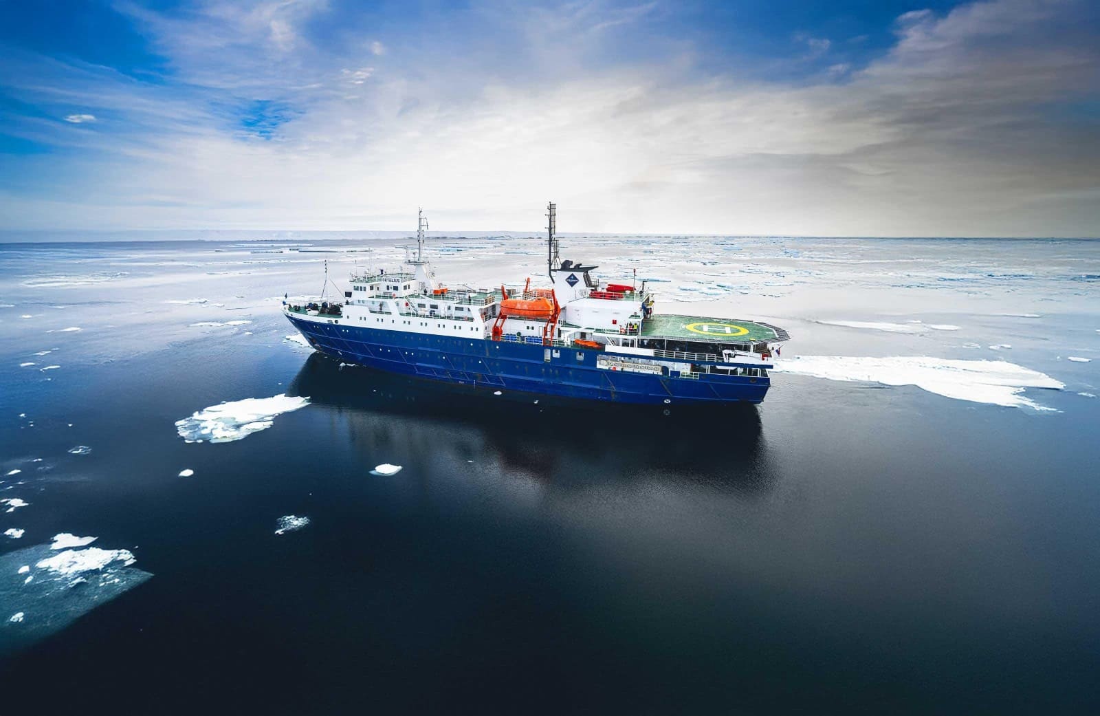 Expedition vessel anchored in a calm Antarctic bay surrounded by towering icebergs and snow-covered peaks under pale polar light, extreme off-the-beaten-path honeymoon, editorial photography