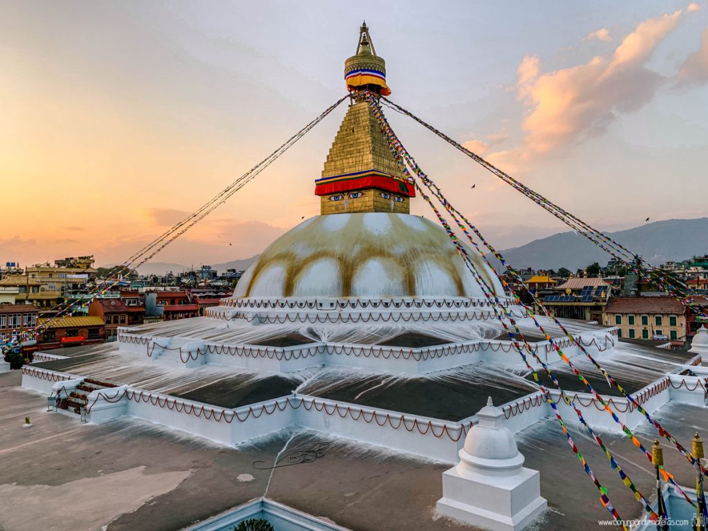 Boudhanath Stupa in Kathmandu Nepal with prayer flags radiating from the golden spire and monks walking the kora in warm morning light, sacred cultural honeymoon, editorial photography
