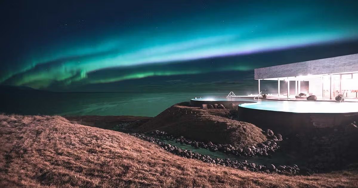 Northern lights glowing green above a geothermal hot spring in Iceland with steam rising into the cold night air and snow-dusted volcanic terrain, Iceland aurora honeymoon, editorial photography