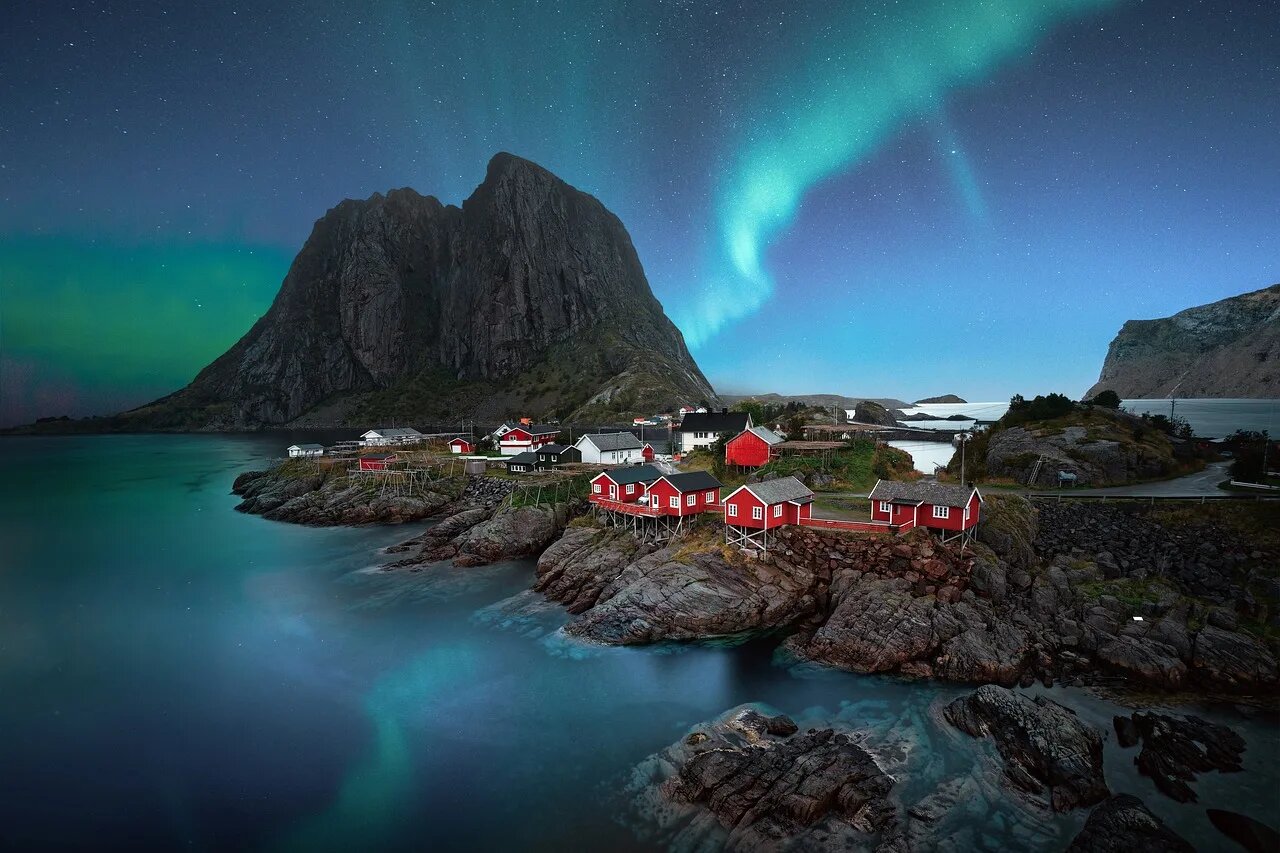 Northern lights sweeping across a dark sky above the snow-covered Lofoten Islands in Norway with fishing villages and fjord reflections below, Norway aurora honeymoon, editorial photography