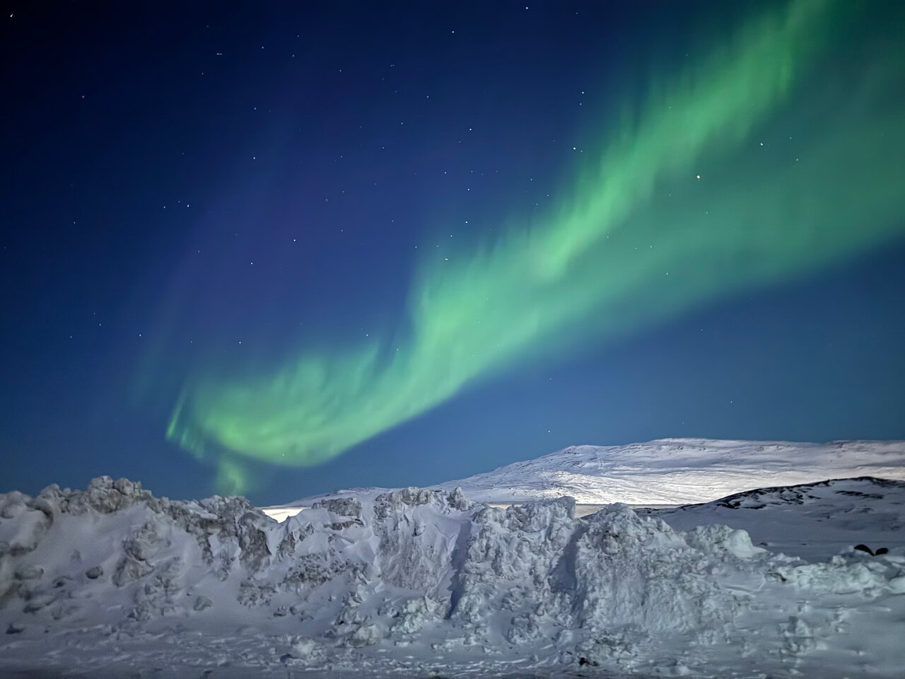 Northern lights illuminating a vast icy landscape near Ilulissat Greenland with massive icebergs floating in dark Arctic waters under a green and violet aurora sky, Greenland aurora honeymoon, editorial photography