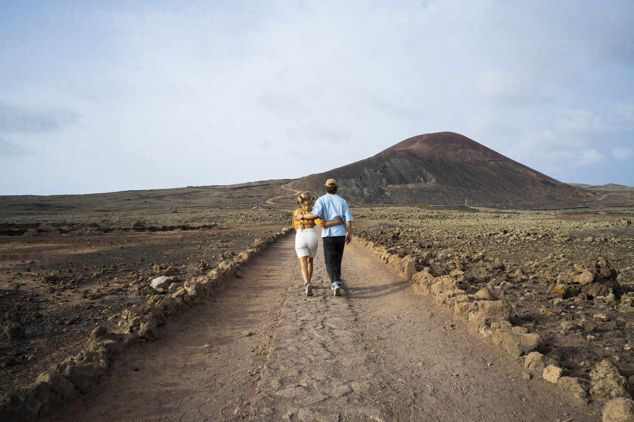 Couple hiking across a dramatic volcanic landscape with a glacier visible in the distance under moody skies, adventure honeymoon energy and scale, editorial travel photography