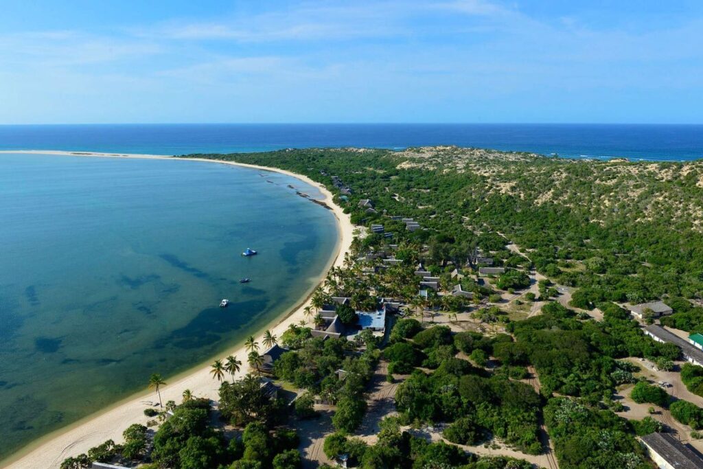 Panoramic Mozambique coastline at golden hour with turquoise water meeting white sand and tropical vegetation, honeymoon dest