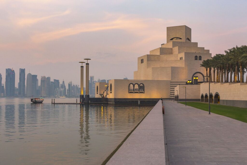 Panoramic view of Doha Qatar skyline at golden hour with Museum of Islamic Art in foreground and Arabian Gulf reflecting warm