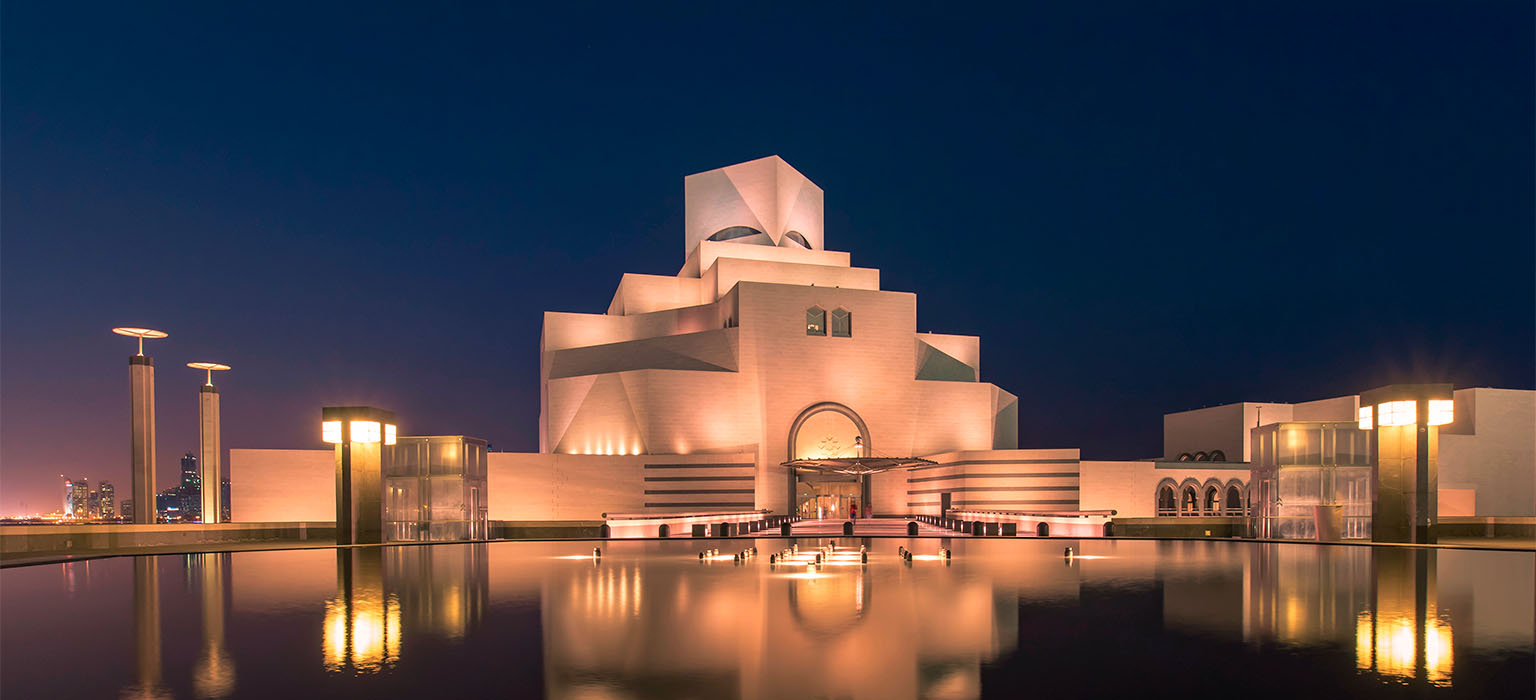 Museum of Islamic Art in Doha Qatar at golden hour with geometric facade reflecting warm light on calm waterfront promenade, Middle East cultural honeymoon, editorial travel photography