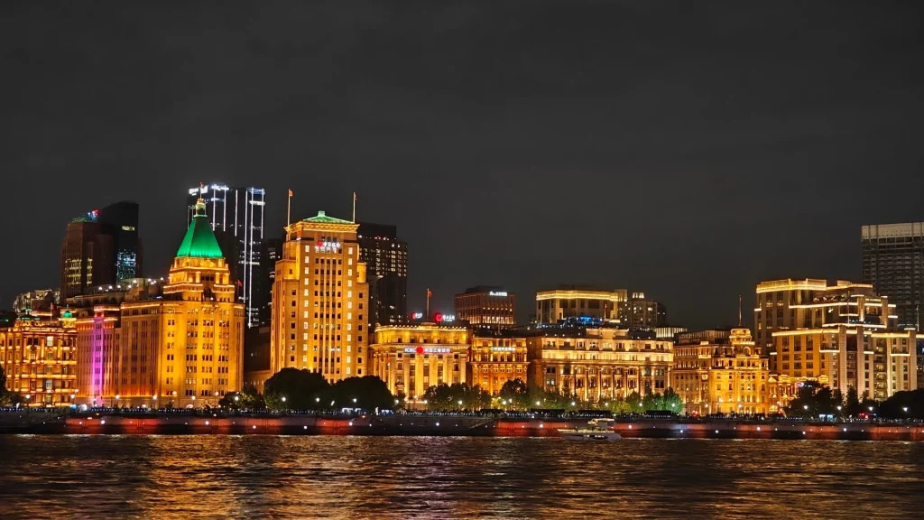 The Bund waterfront promenade in Shanghai at twilight with Art Deco buildings illuminated and Pudong skyline reflecting across the Huangpu River, luxury China honeymoon, editorial photography