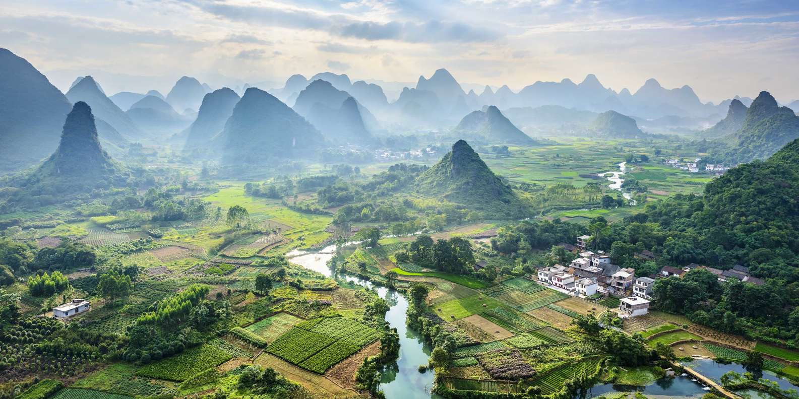 Yangshuo countryside in Guilin China with lush green rice paddies and dramatic karst limestone peaks under soft afternoon light, rural landscape honeymoon, editorial photography