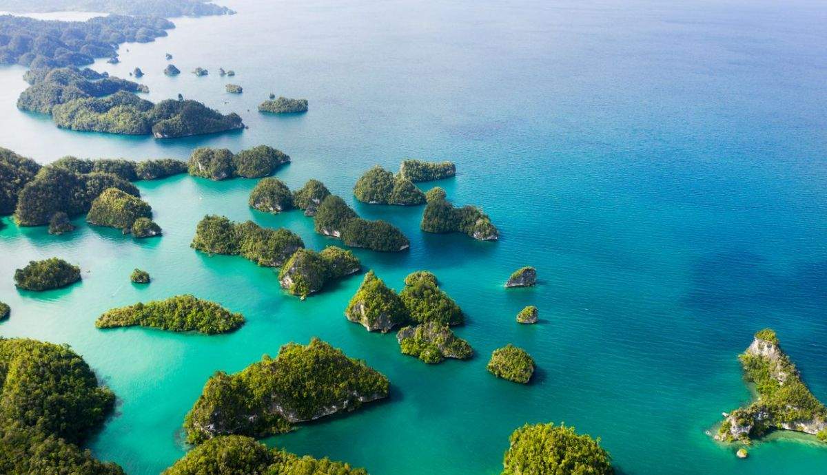 Aerial view of Indonesian archipelago islands with turquoise channels between lush green volcanic landmasses and scattered traditional boats, luxury honeymoon destination, editorial travel photography