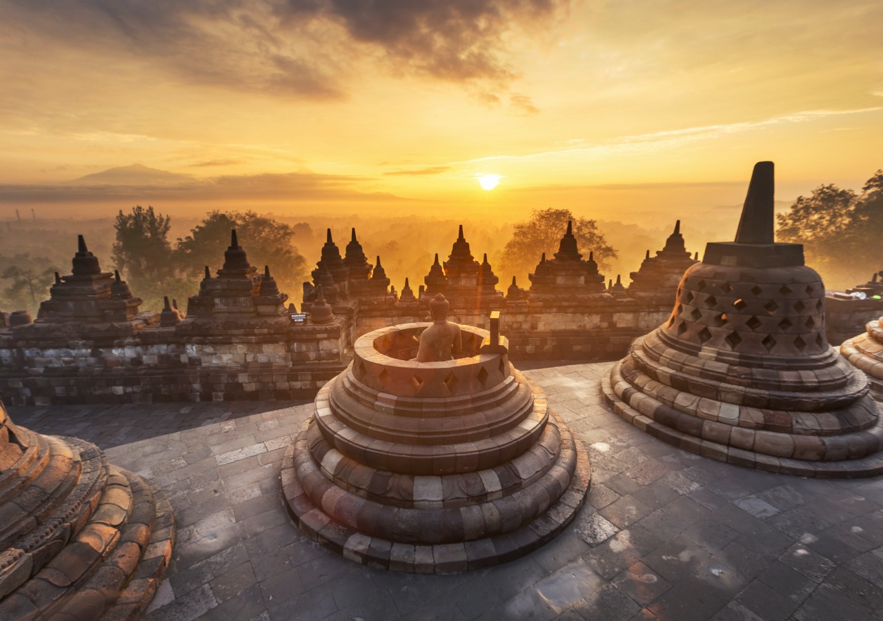 Borobudur temple at sunrise with volcanic silhouette and morning mist drifting across the Kedu Plain in Java Indonesia, UNESCO World Heritage cultural honeymoon, editorial photography