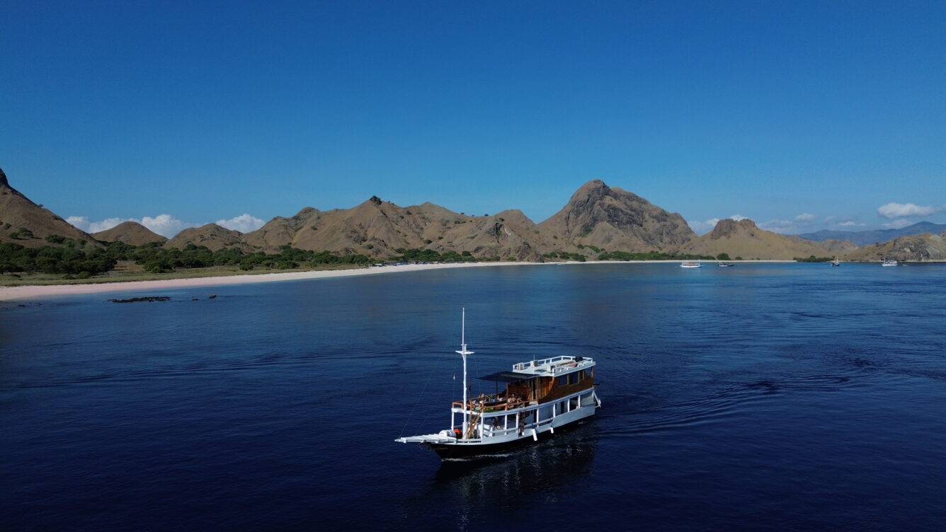 Komodo National Park turquoise bay with traditional wooden phinisi sailing boat anchored near volcanic green hills, Indonesian archipelago honeymoon, editorial travel photography