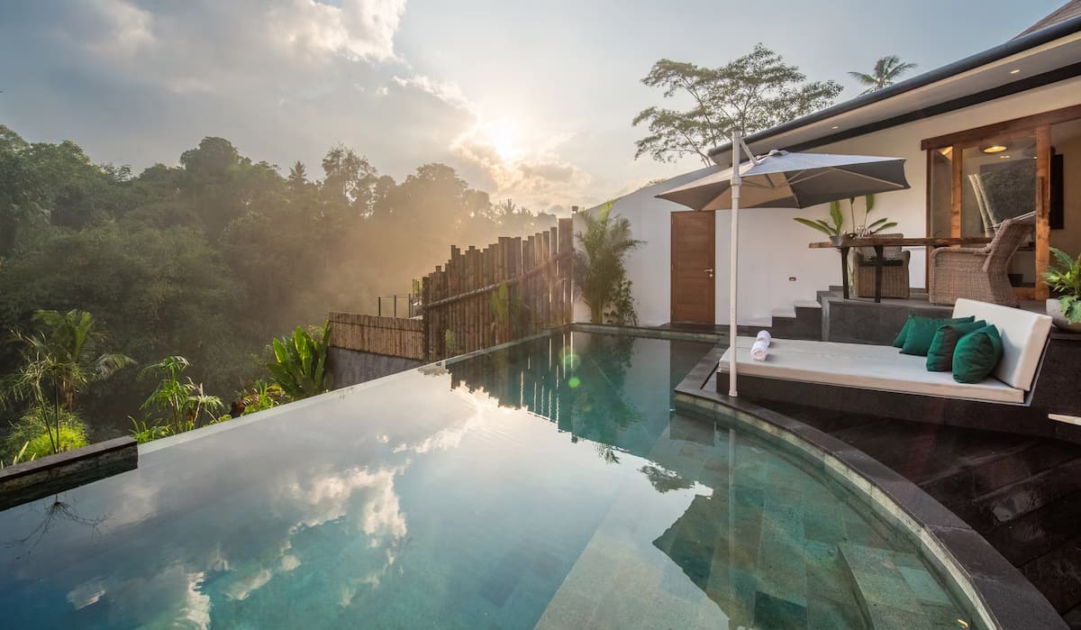 Infinity pool overlooking Ayung River valley in Ubud Bali surrounded by tropical jungle canopy and morning mist, luxury resort setting, editorial travel photography