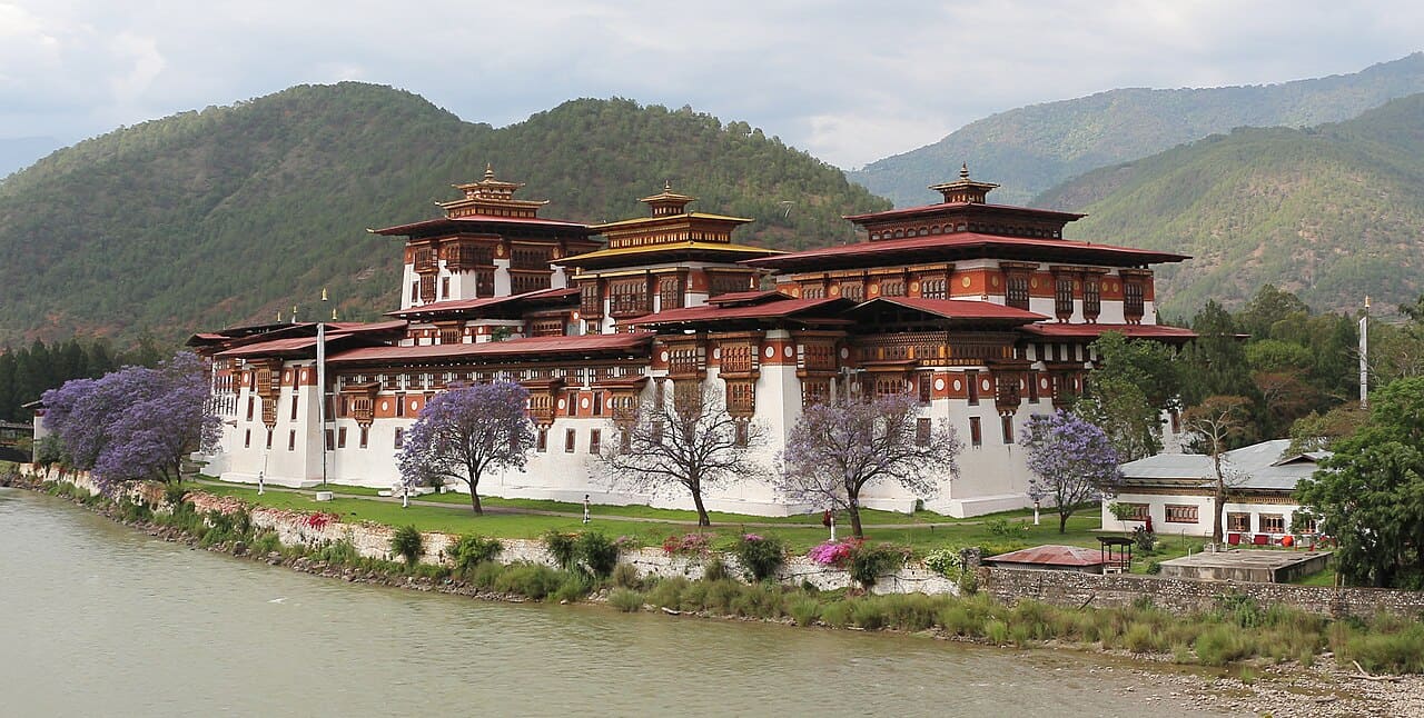 Punakha Dzong fortress at the confluence of two rivers in Bhutan with traditional whitewashed walls and golden rooftops surrounded by forested Himalayan hillsides, cultural honeymoon, editorial photography