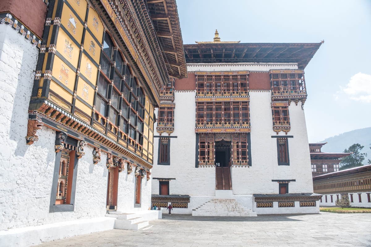 Traditional Bhutanese architecture in Thimphu with colourful painted wooden facades and prayer wheels along a quiet street with Himalayan peaks in the background, Bhutan honeymoon, editorial photography