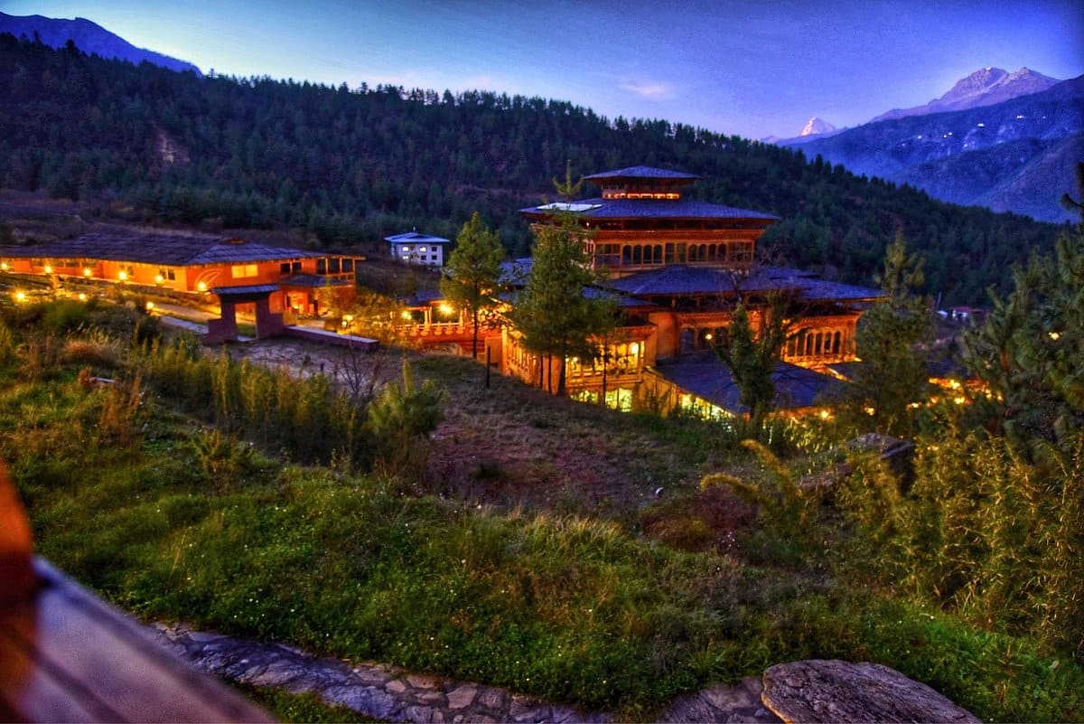 Luxury mountain lodge in Bhutan with traditional Bhutanese architecture and floor-to-ceiling windows overlooking a misty Himalayan valley at sunrise, Six Senses or Amankora style, editorial photography