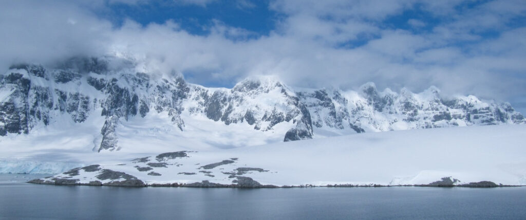 Panoramic view of Antarctic Peninsula with massive glaciers, icebergs and dark polar water under dramatic cloudy sky, expedit