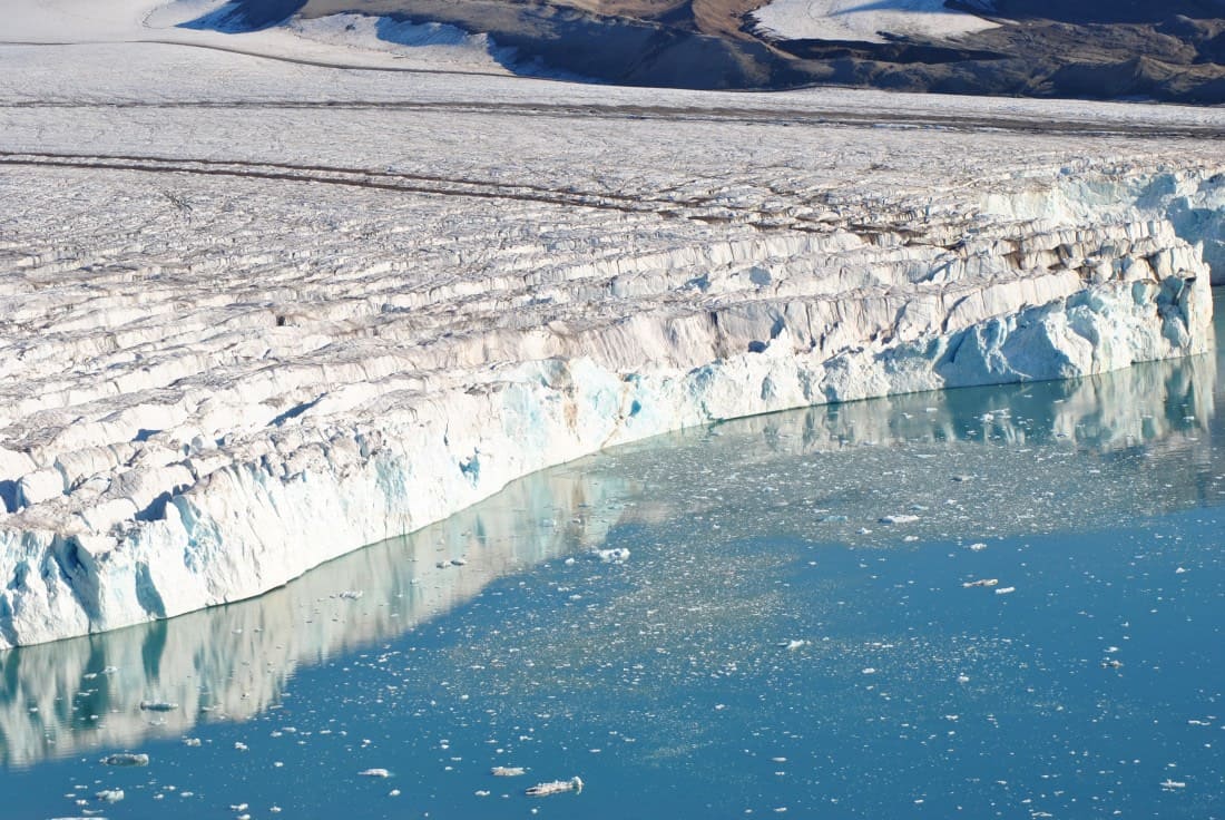 Antarctic Peninsula glaciers and icebergs reflected in perfectly still dark polar water with a zodiac boat approaching in the distance, expedition honeymoon, editorial travel photography