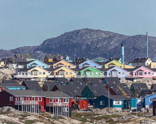 Panoramic view of Ilulissat Icefjord Greenland with massive icebergs in deep blue water and colourful town houses on the hill