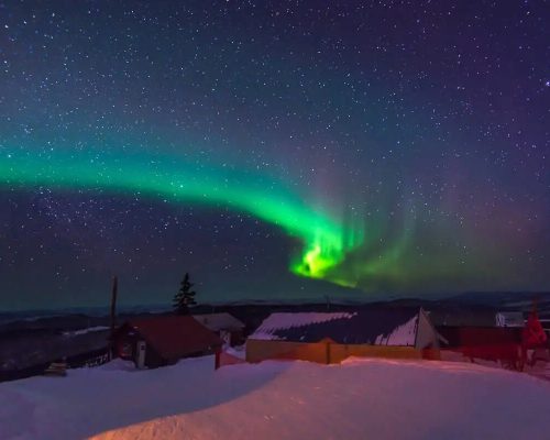 Northern lights honeymoon editorial image with vivid green aurora borealis stretching across a dark Arctic sky above a snow-c