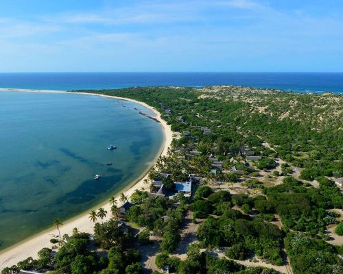 Panoramic Mozambique coastline at golden hour with turquoise water meeting white sand and tropical vegetation, honeymoon dest