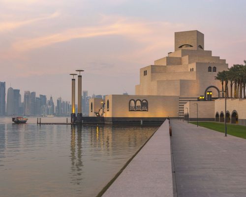 Panoramic view of Doha Qatar skyline at golden hour with Museum of Islamic Art in foreground and Arabian Gulf reflecting warm