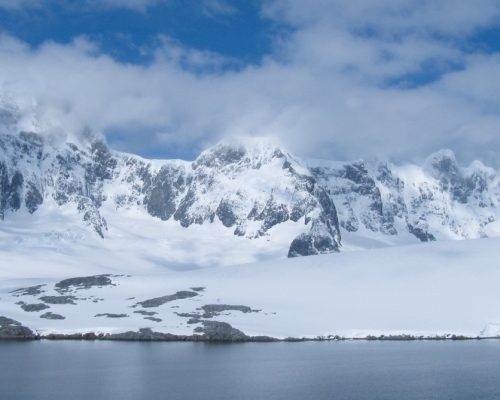 Panoramic view of Antarctic Peninsula with massive glaciers, icebergs and dark polar water under dramatic cloudy sky, expedit
