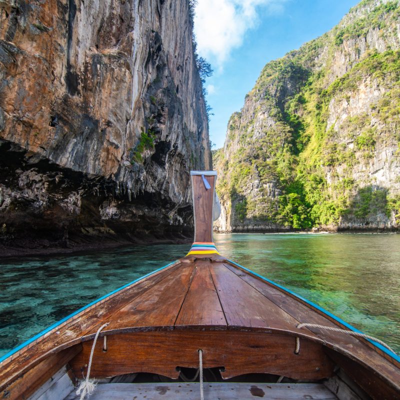 Traditional wooden longtail taxi boat nose with decoration flowers and ribbons at Maya Bay beach against steep limestone hills. Main Thailand tourist attraction background, Ko Phi Phi Island SSUCv3H4sIAAAAAAAACpyRy47DIAxF9yPNP0SsGymP5tH+SjULB0iCSqACMqNR1X8fA6FiPTt8bF/7mufnR1GQCayg5Fo8fYSxkHK3zoATWiGuTgc3XDFucsKZcNoIkDmcwNFVwcYRql1Kj18hSawDt1tu/bADUXB8QY0I3xJxo1uMi5QISezAFCGnjNl9CiyhKP6vzvj4Sm5g4Yr+hoUzI4ZLDtHILZaS+4/jZsutwc6Ezlx9awrSF7SZ0sMIKtSStWm3hiunNqp35Yxf4b05kVo/YJL+xDNq8sRXsBbLWeLZIIp/qrdsjtIuGDhUCcOf8GHdNm3d1fVwHoehH8fmchTE31sF6oR1khDG9C5Ybl34DQgdmrbrR1pWfd2XZ9rMJYwDL+eBTdBeqrpqOjz86w8AAP//AwArpjtvhwIAAA==