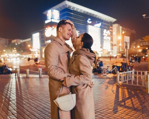 young couple showing affection while hugging in the middle of Beijing China. Couple wearing winter coats and white sneakers as they are hugging in the middle of the street in Beijing China.